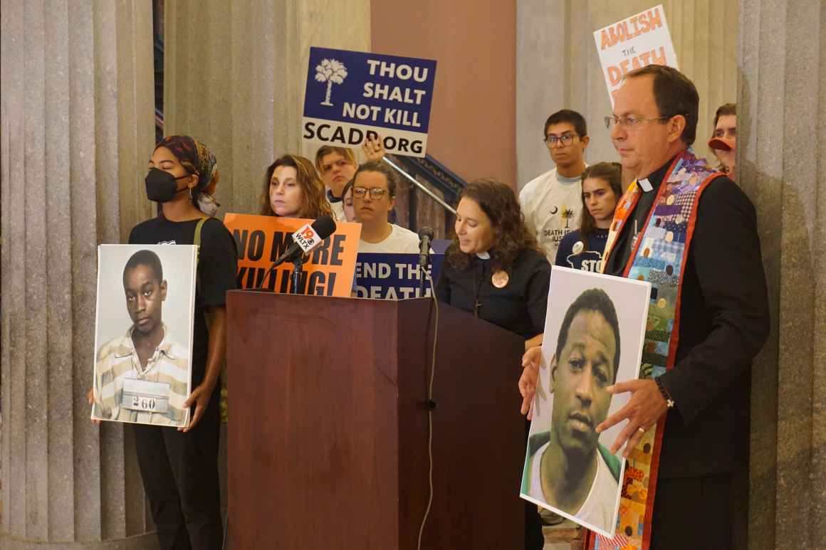 Anti-death penalty activists including clergy stand behind a lectern, beside some columns inside the South Carolina State House lobby.