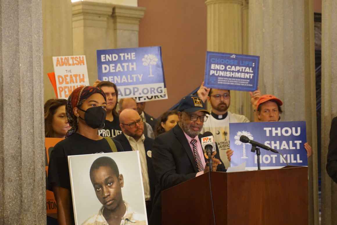 Anti-death penalty activists including clergy stand behind a lectern, beside some columns inside the South Carolina State House lobby.